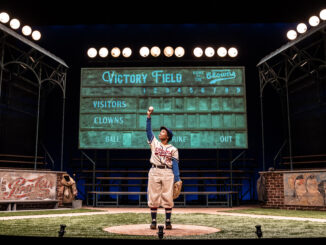 Toni holds a baseball up in the air triumphantly